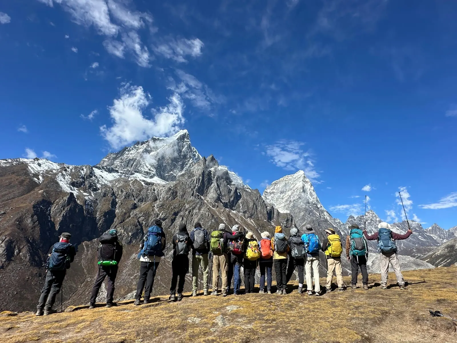 A trekking group lined up on a high ridge, looking out at rocky snow-capped peaks